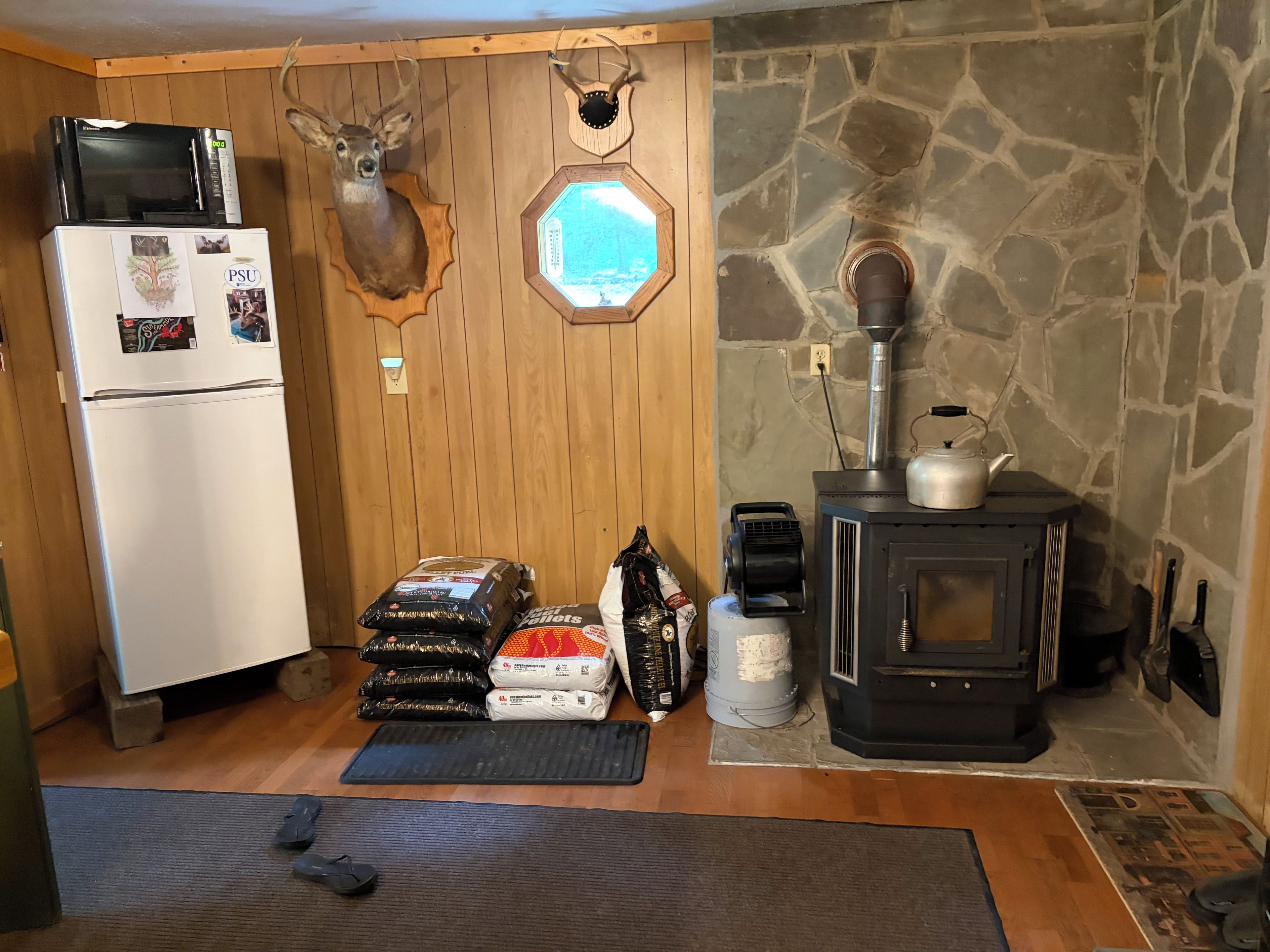A compact kitchen with a refrigerator, microwave, and stove, wooden walls, stone accents, and a deer head decoration.