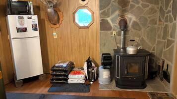 A compact kitchen with a refrigerator, microwave, and stove, wooden walls, stone accents, and a deer head decoration.