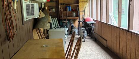 A wooden interior with a table and chairs, a window, and various items on shelves.