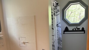 Une salle de bain comprenant des toilettes, un rideau de douche, une fenêtre et une étagère fixée au mur, ornée d’un motif représentant un cerf.