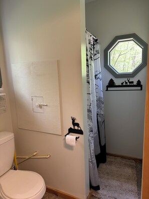 Baño con inodoro, cortina de ducha, ventana y repisa de pared con un adorno de ciervo.