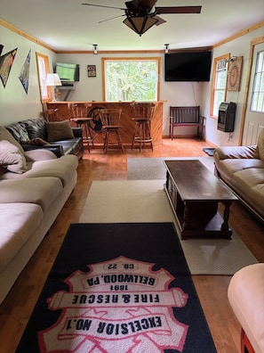 A living room with a fireplace, a television, a wooden bar, and a large window. - Cozy cabin nestled the woods (Warriors mark)