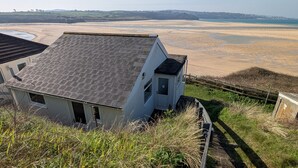 Une maison située sur la côte, dotée d’un toit en pente, d’une petite dépendance attenante et offrant une vue sur la plage et la mer.