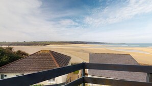 Une vue sur la plage depuis un balcon doté d’une balustrade en bois, avec un ciel dégagé et des collines à l’horizon.