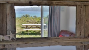 A rustic wooden-framed window overlooking a grassy area with a picnic table and a view of the sea.