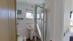 A compact bathroom with a glass shower enclosure, a sink, and a toilet.