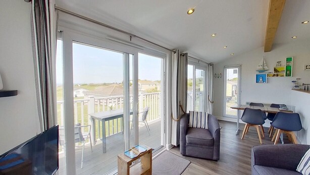 A spacious living room with a large sliding glass door leading to a balcony, a dining area with a table and chairs, and a cozy seating area with a sofa.