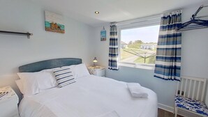 A bedroom with a bed, a nightstand, a lamp, a window with curtains, and a view of the outside.