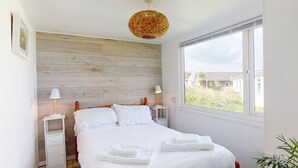 Ein Schlafzimmer mit einem hölzernen Kopfteil, einem großen Fenster und Blick ins Freie.