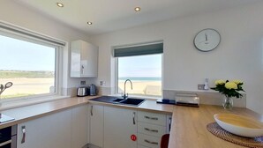 A modern kitchen with a sink, cabinets, and a window overlooking a beach. - B27 The Lair, Riviere Towans (Hayle)