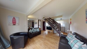 Un vaste espace de vie doté d’un plancher en bois, d’un escalier, d’une cuisine et d’une chambre à coucher visible à travers une porte ouverte.