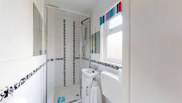 Een badkamer met een douche, een wastafel en een raam.