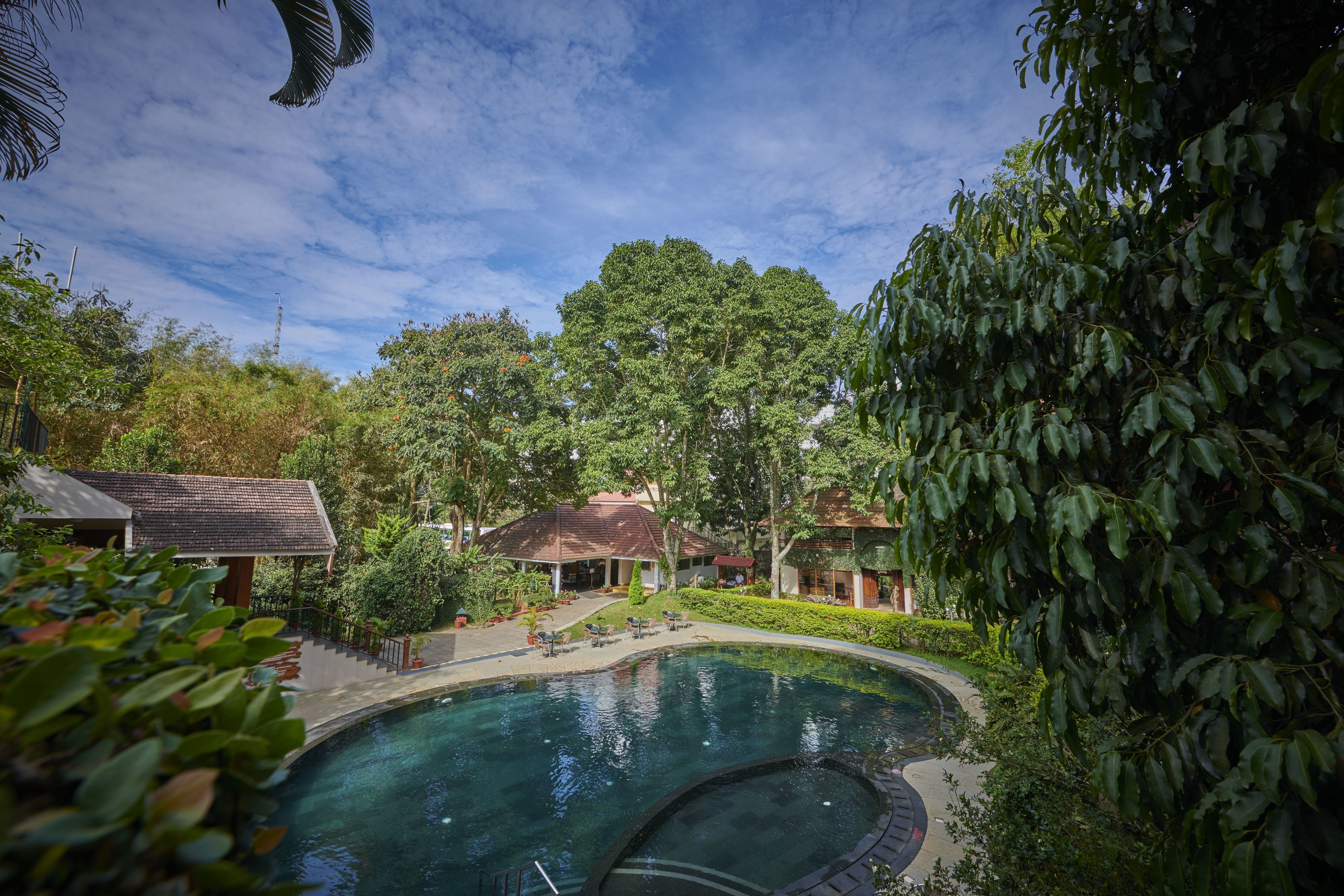 A swimming pool surrounded by lush greenery and buildings with red-tiled roofs.
