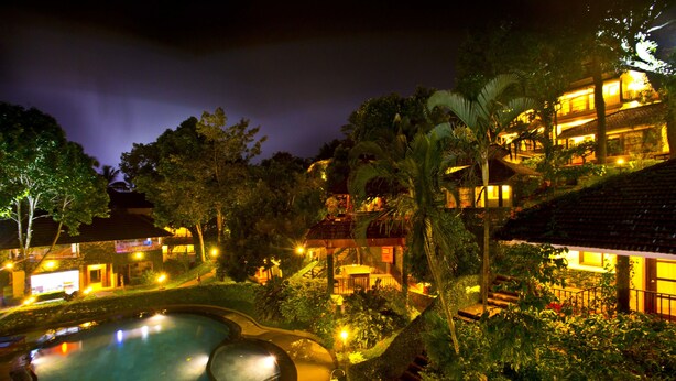 A resort with a swimming pool, lush greenery, and illuminated buildings at night. - Cardamom County by Xandari (Peermade)