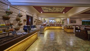 A hotel lobby with a long counter, potted plants, and a decorative ceiling. - Cardamom County by Xandari (Peermade)