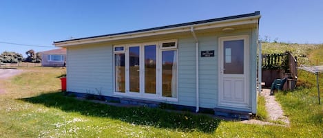 En liten, envåningsbyggnad med vit fasad och en dörr med ett fönster. På dörren finns en skylt med texten ”42, Sjöjungfruns viloplats”.