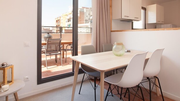 Un appartement moderne doté d’un coin repas, de grandes portes-fenêtres coulissantes, d’une cuisine et offrant une vue sur les bâtiments environnants.