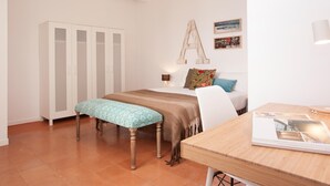 Une chambre à coucher comprenant un lit, une table en bois, un banc, une armoire et un mur orné d’une grande lettre et de tableaux.