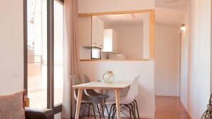 Une pièce moderne et bien éclairée, avec une table à manger, des chaises et un canapé. Un grand miroir reflète l’espace cuisine.