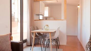 Una habitación moderna y bien iluminada con una mesa de comedor, sillas y un sofá. Un espejo grande refleja la zona de la cocina.