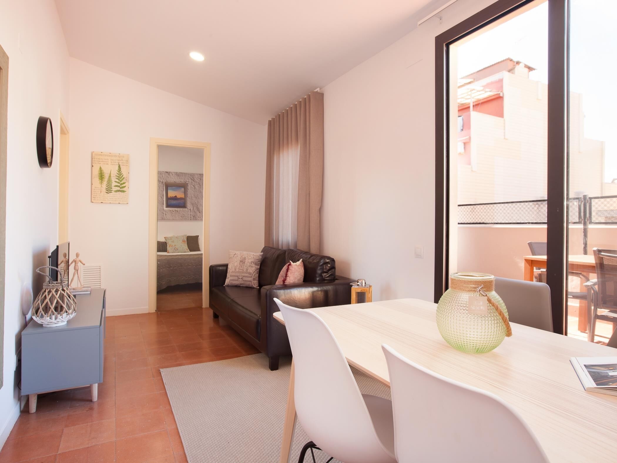 Una sala de estar moderna con un sofá, una mesa de comedor con sillas, una pequeña mesita auxiliar y vistas al exterior a través de un amplio ventanal.