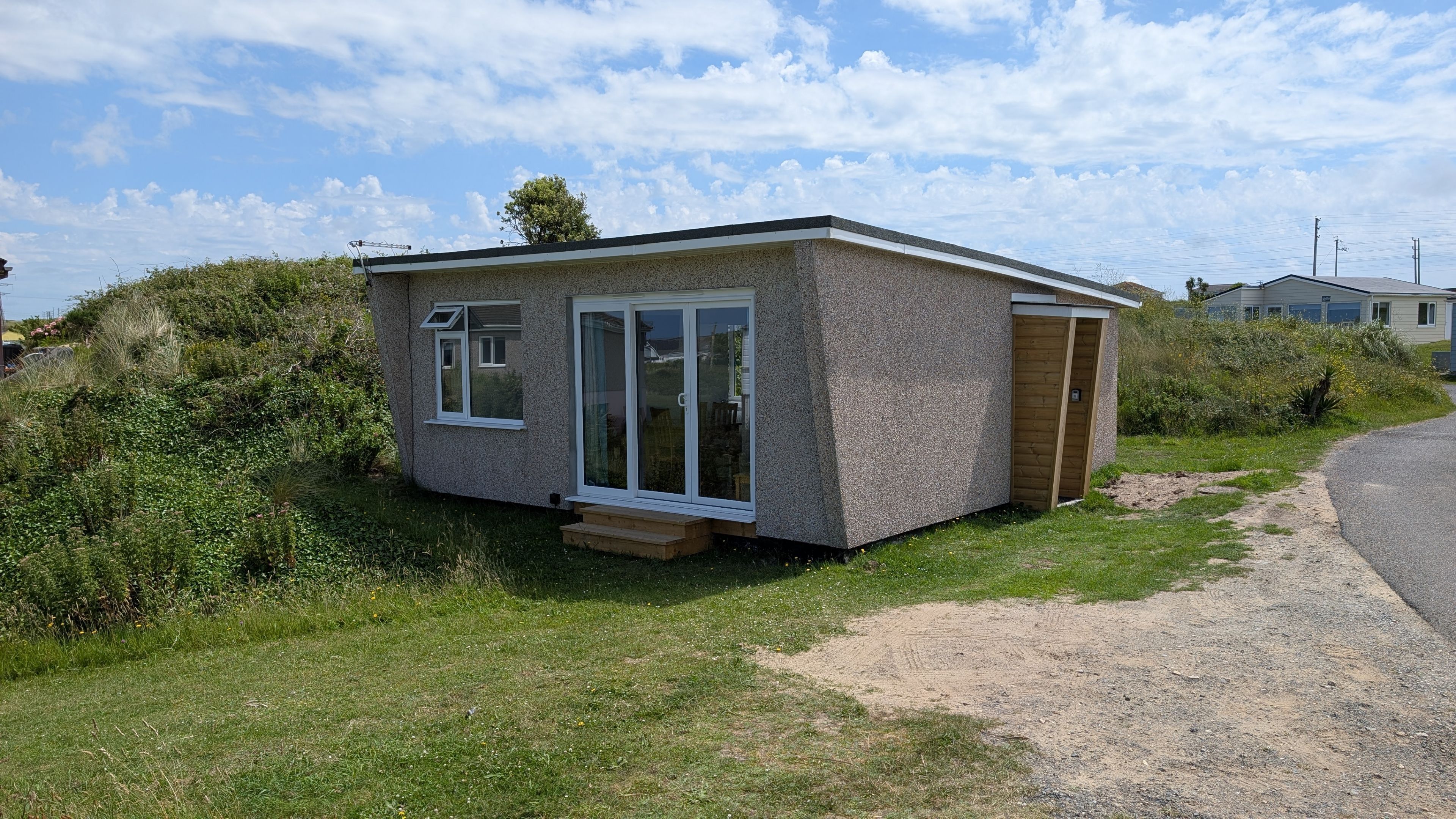 A small, single-story building with a sloped roof, a front door, and a sliding glass door.