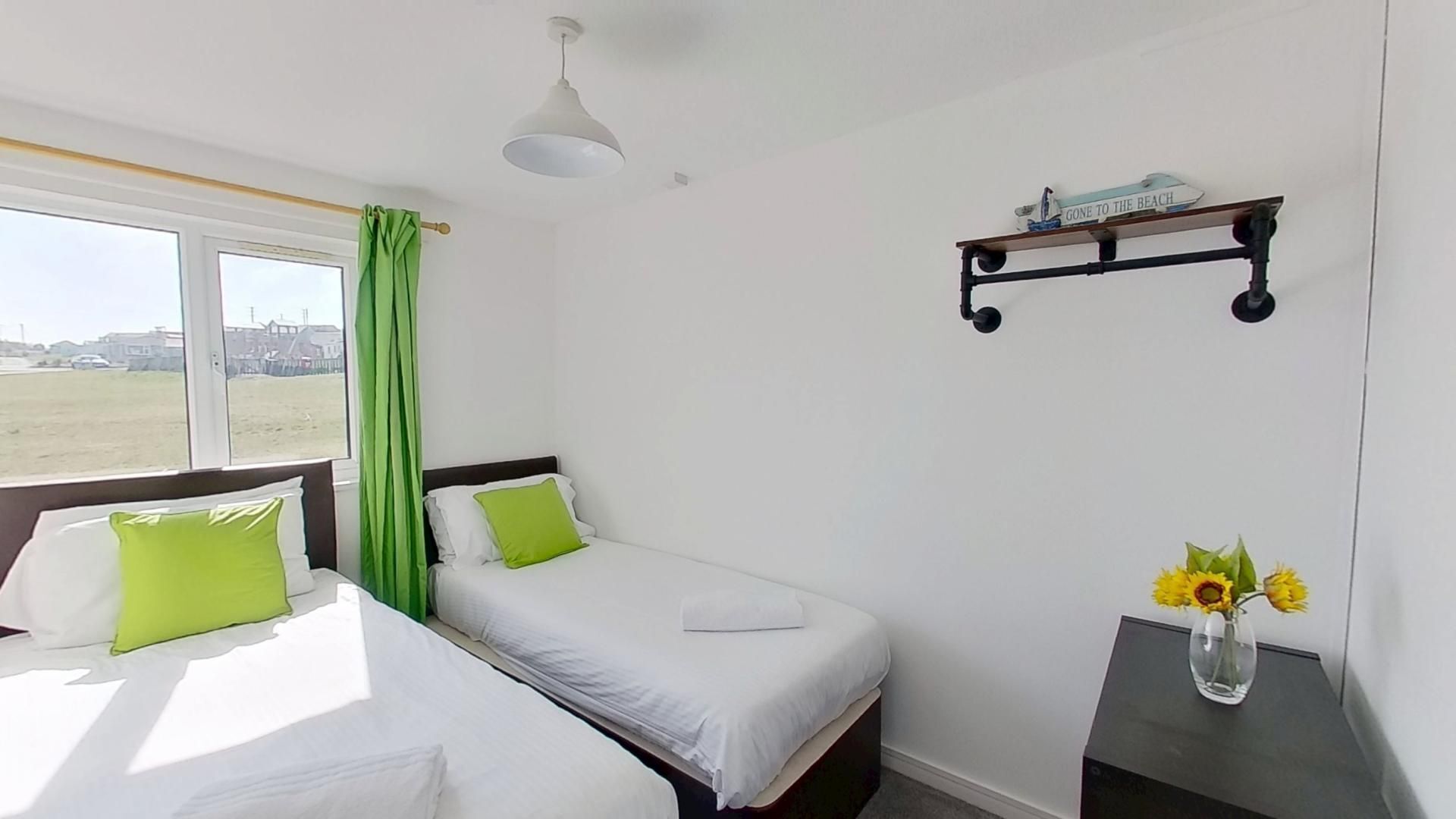 A hotel room with two beds, a window with a view of the beach, a shelf with a sign, and a vase with flowers.