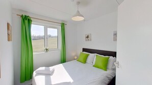 Camera da letto con un letto, tende verdi, una finestra e un punto luce a parete.