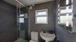 Une salle de bain avec une douche à parois de verre, des toilettes, un lavabo et une fenêtre.