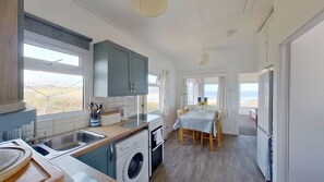 Une cuisine compacte équipée d’un lave-linge, un coin repas avec une table et des chaises, et une vue sur la plage par les fenêtres.