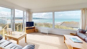 Un salon spacieux doté de grandes fenêtres, d’un téléviseur à écran plat et offrant une vue sur la plage.
