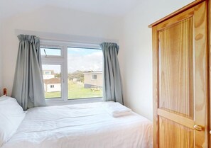 Une chambre avec une grande fenêtre, une armoire en bois et un lit soigneusement fait.