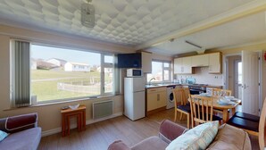 Cocina compacta con microondas, refrigerador y pileta. Hay un comedor con mesa y sillas, y una sala de estar con sofá.