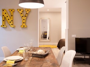 A dining area with a wooden table set for four, a television, and a mirror reflecting the room. - Stylish apartment in city center B3 (Barcelona)