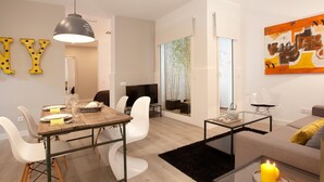 A modern living room with a dining area, a black and white abstract painting, and a large window with a view of bamboo. - Stylish apartment in city center B3 (Barcelona)