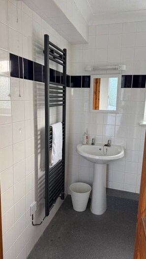 A bathroom with white tiles, a black towel rack, a sink, and a mirror.