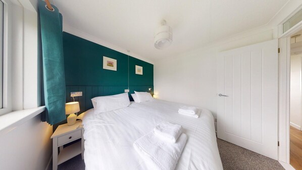 A hotel room with a large bed, two bedside tables, a nightstand, a window with curtains, and a door.