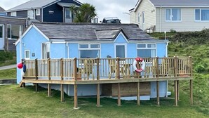 A small, single-story house with a wooden deck and a lifebuoy on the railing. - E08 Boness (E8), Riviere Towans (Hayle)
