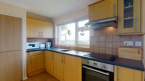A kitchen with wooden cabinets, a microwave, a toaster, a sink, and a window with a view. - D55 Wheal Lucy, Riviere Towans (Hayle)