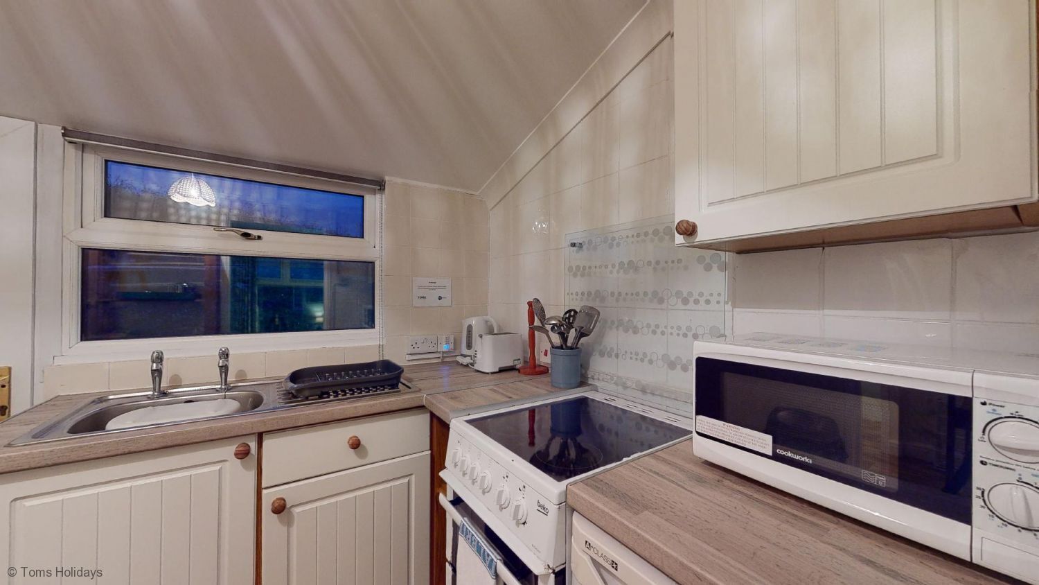 Une cuisine avec des meubles blancs, une cuisinière, un four à micro-ondes, un évier et une fenêtre donnant sur un beau paysage.