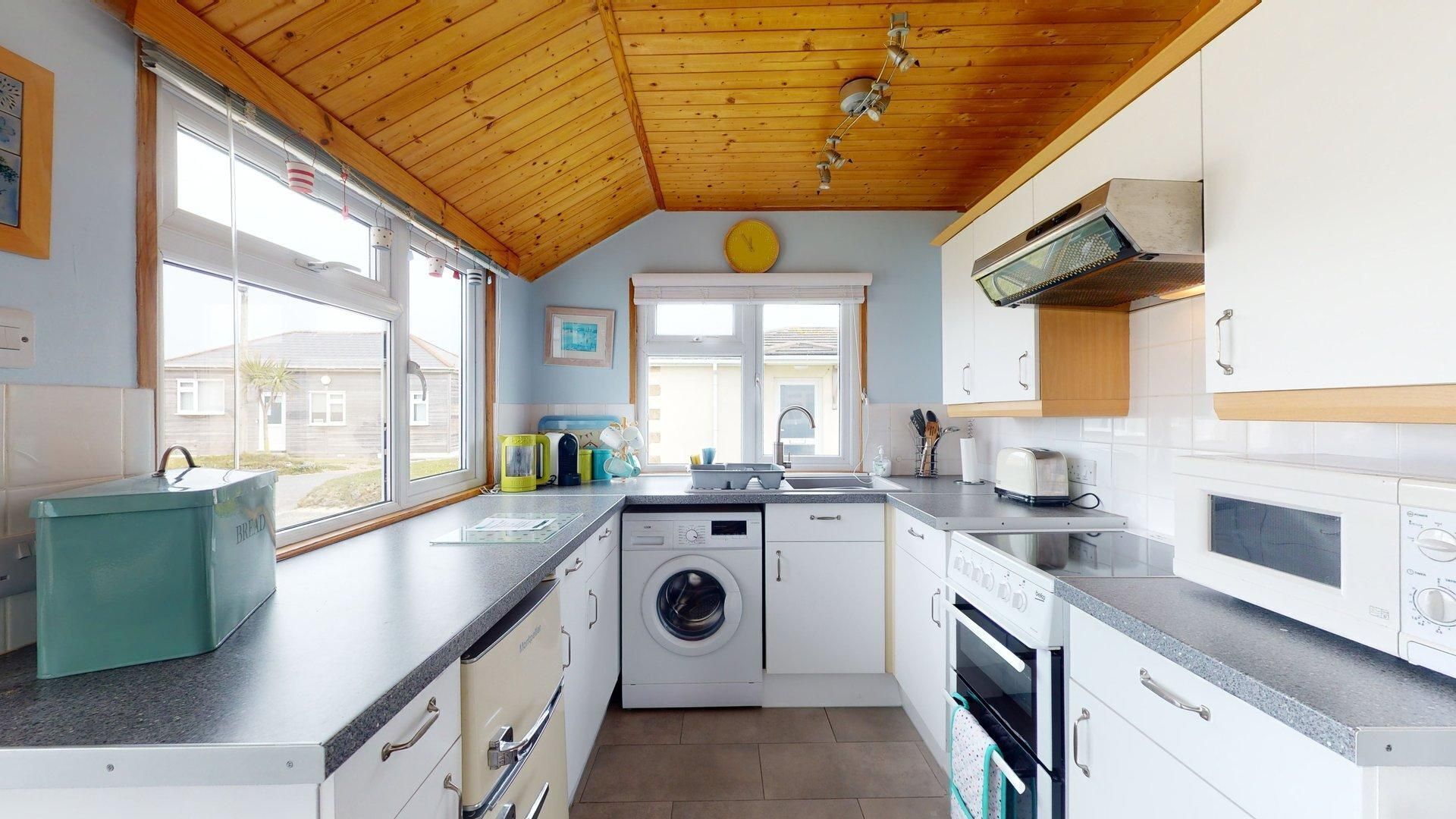 A compact kitchen with a washing machine, oven, and a window with a view of houses.