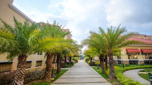 A pathway lined with palm trees leading to a building with a red awning. - SR Vacation Rental - San Remo Oasis (Cebu City)