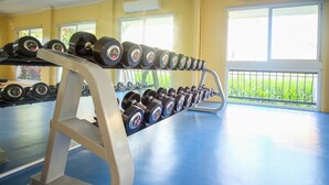 A gym with a blue floor, a rack of dumbbells, and windows with a view of greenery. - SR Vacation Rental - San Remo Oasis (Cebu City)
