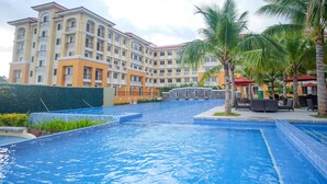 A swimming pool with a tiled edge, surrounded by palm trees and a multi-story building with balconies. - SR Vacation Rental - San Remo Oasis (Cebu City)