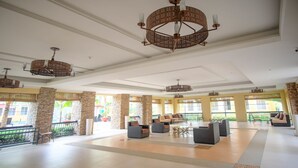 A spacious lobby with high ceilings, multiple seating areas, and large windows offering views of the outside. - SR Vacation Rental - San Remo Oasis (Cebu City)