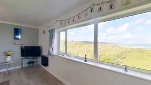 A room with a large window, a flat-screen TV, a small table with a vase, and a decorative string above the window. - B38 Delamar, Riviere Towans (Hayle)