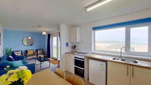 A compact living space with a kitchenette, a dining area, and a seating area with a view of the sea. - B52 Oyster, Riviere Towans (Hayle)