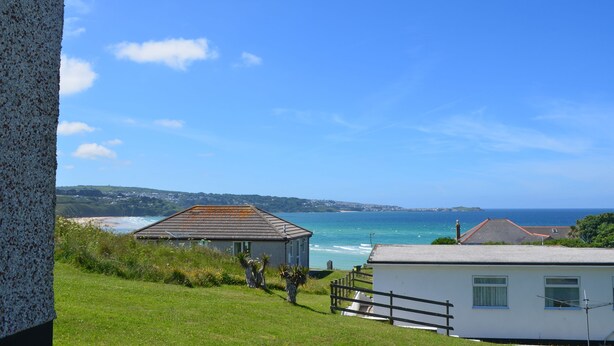 A coastal view with a grassy area, a small building, and a white house with a view of the sea. - B52 Oyster, Riviere Towans (Hayle)