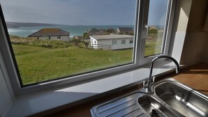 A kitchen with a large window overlooking a grassy area and houses by the sea. - B52 Oyster, Riviere Towans (Hayle)