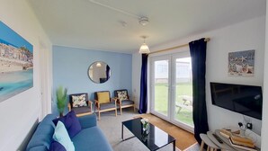 A living room with a sofa, two armchairs, a coffee table, a TV, and a large window with curtains. - B52 Oyster, Riviere Towans (Hayle)